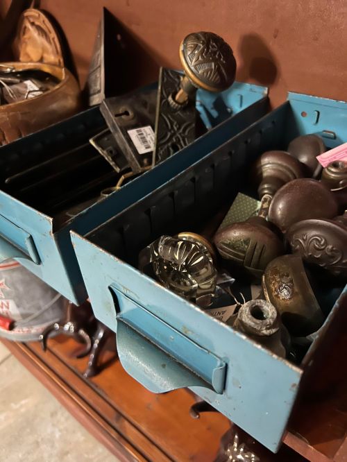 Two blue metal boxes filled with various antique knobs and hardware pieces, resting on a wooden surface.