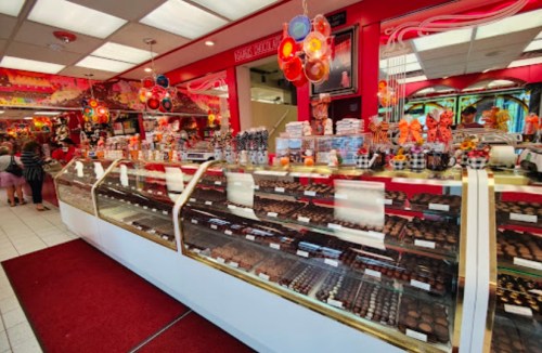 A colorful candy shop display filled with various chocolates and sweets, with customers browsing in the background.