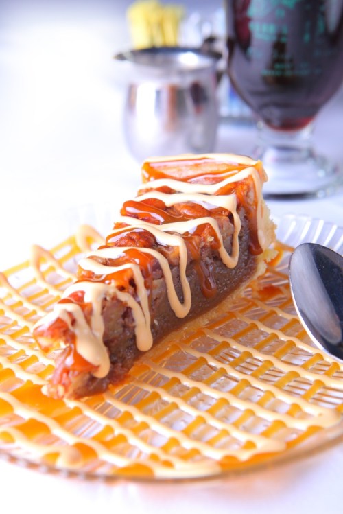 A slice of cake drizzled with caramel and cream on a decorative plate, with a spoon beside it.