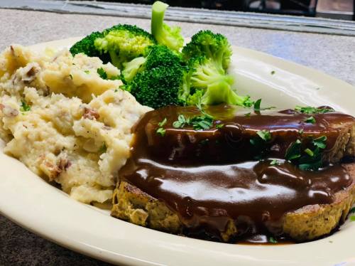 A plate of meatloaf with gravy, mashed potatoes, and steamed broccoli, garnished with parsley.