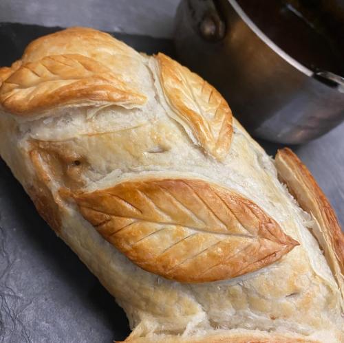 Golden-brown pastry with leaf designs, resting on a slate surface next to a small pot.