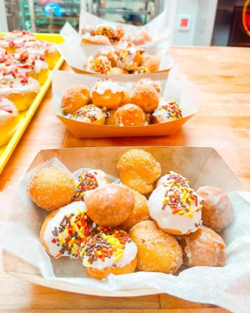 A wooden tray filled with assorted mini donuts topped with icing and colorful sprinkles.
