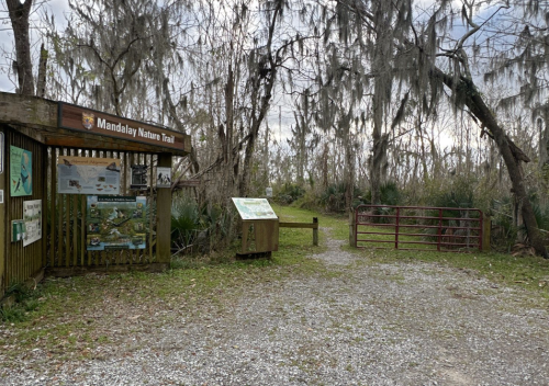 Entrance to Mandalay Nature Trail with informational signs and a gravel path leading into a wooded area.