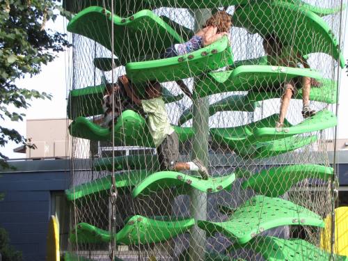 Children climbing on a green, wavy climbing structure with a net, enjoying outdoor play at a park.