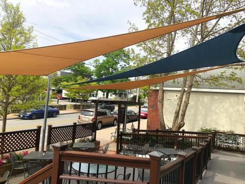 Outdoor seating area with shaded canopies, trees, and parked cars in the background on a sunny day.