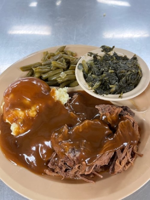 A plate of food featuring mashed potatoes with gravy, tender beef, green beans, and collard greens.