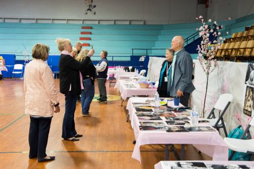 A group of people interacting at tables decorated with pink tablecloths in a gymnasium setting.