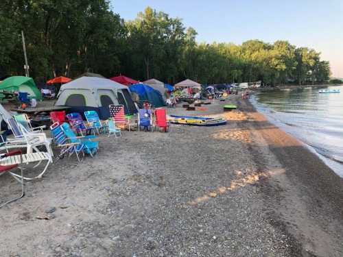 A beach scene with tents, colorful chairs, and kayaks along the shore, surrounded by trees and calm water.