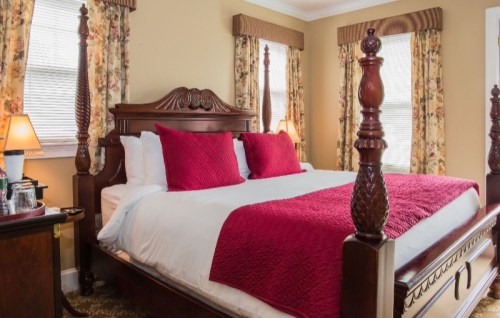 Cozy bedroom featuring a large wooden bed with red pillows, floral curtains, and warm lighting.