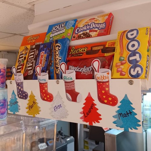 A shelf displaying various candies and snacks, decorated with colorful stockings and names.