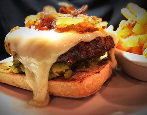 A juicy burger topped with melted cheese, caramelized onions, and avocado on toasted bread, served with crispy fries.