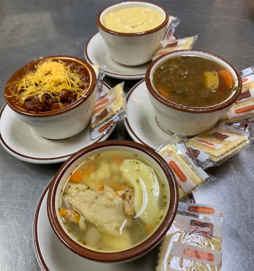 Four bowls of soup and chili, topped with cheese, served with crackers on the side.