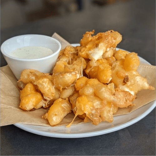 A plate of golden, crispy fried cheese curds served with a small bowl of dipping sauce.