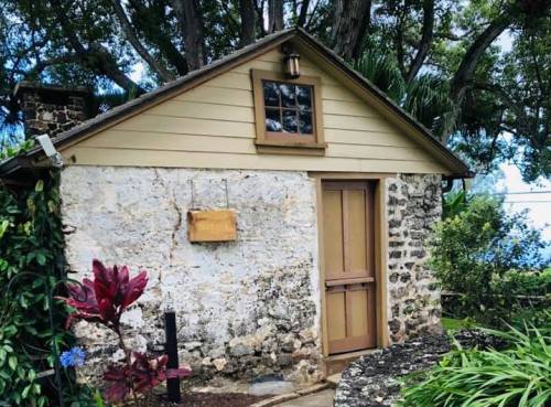A rustic stone and wood cottage surrounded by greenery, featuring a wooden door and a small window.