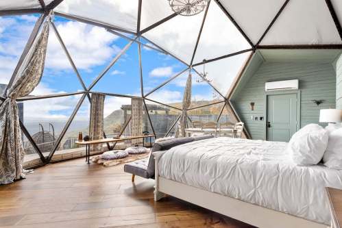 A modern geodesic dome bedroom with large windows, offering a scenic view of the outdoors and stylish interior decor.