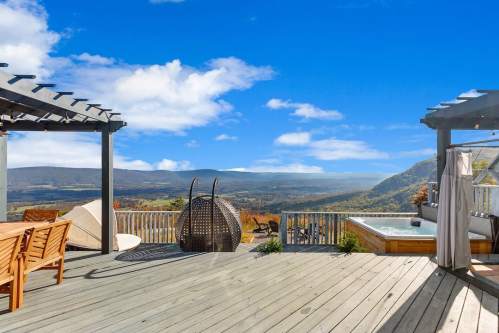 Scenic outdoor deck with seating, a hot tub, and panoramic mountain views under a clear blue sky.