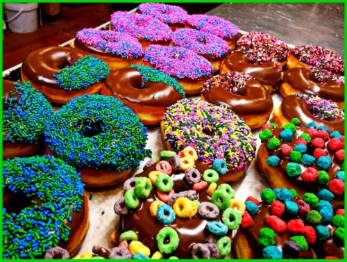 A colorful assortment of chocolate-covered donuts topped with vibrant sprinkles and cereal pieces.