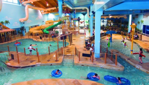 Indoor water park featuring slides, pools, and guests enjoying floating on tubes in a tropical-themed environment.
