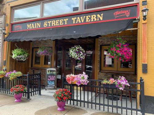 Exterior of Main Street Tavern with colorful flower baskets and planters, inviting entrance under a black awning.