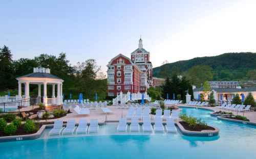 A scenic pool area with lounge chairs, surrounded by greenery and a historic building in the background.
