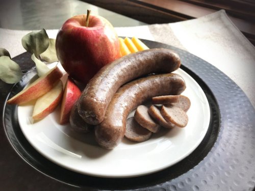 A plate with two sausages, sliced pieces, apple slices, and a whole apple, set on a textured black surface.