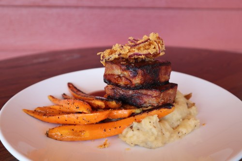A plate of grilled tofu stacked with crispy onions, served with mashed potatoes and roasted carrots.