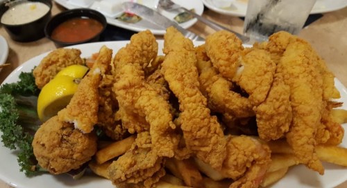 A plate of crispy fried fish fillets and hush puppies served with lemon wedges and fries.