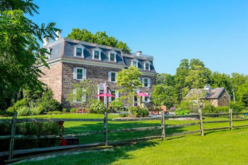 A charming stone house with a green lawn, surrounded by trees and flowers, under a clear blue sky.