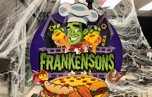 A colorful sign featuring a cartoon chef with green skin, holding pizza and cheese, surrounded by Halloween decorations.