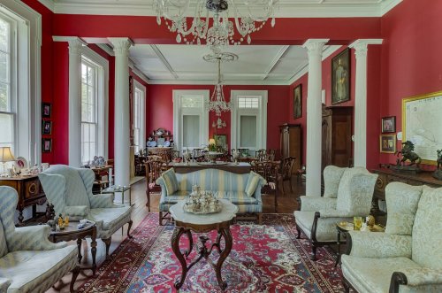 Elegant room with red walls, vintage furniture, a chandelier, and a patterned rug, featuring a cozy seating area.