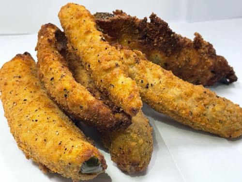 A close-up of crispy, golden-brown fried pickles arranged on a white surface.