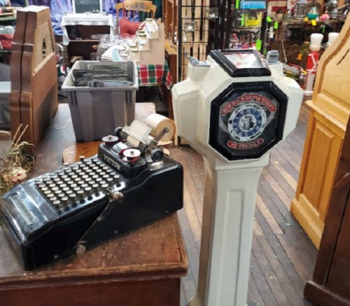 A vintage typewriter next to an old-fashioned gas pump in a rustic shop setting.