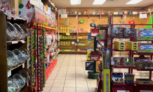 A colorful store aisle filled with candy, toys, and holiday decorations on wooden shelves.
