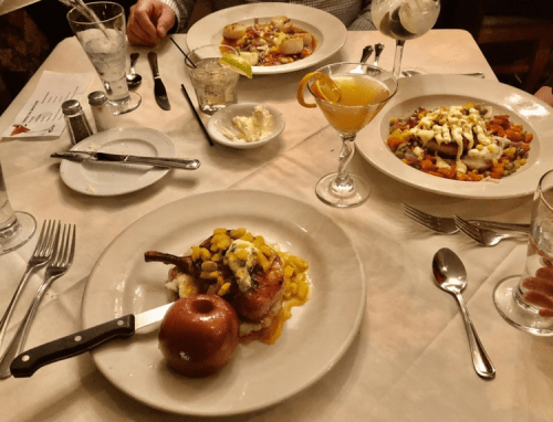 A table set with three plates of gourmet food, including a pork chop with apple, and colorful vegetable dishes.