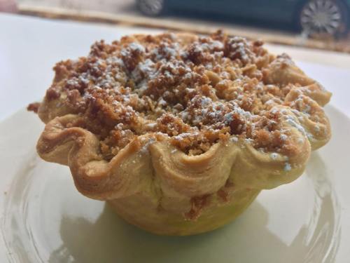 A golden-brown pie with a crumbly topping, dusted with powdered sugar, served on a white plate.