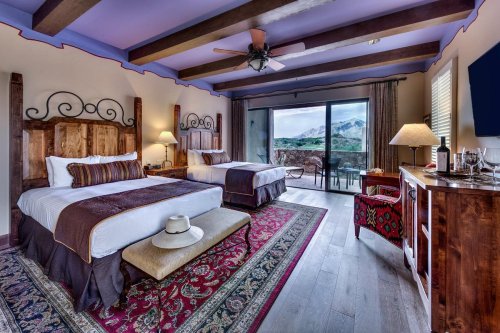 A cozy hotel room with two beds, wooden accents, a view of mountains, and a small seating area.