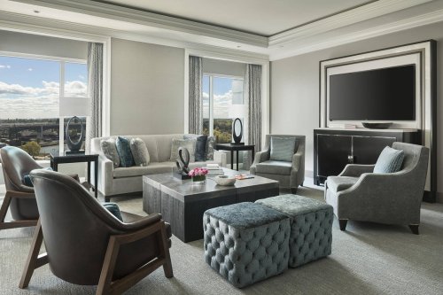 A modern hotel suite featuring a stylish seating area, large windows, and a flat-screen TV.