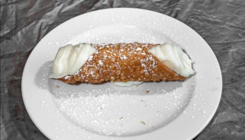 A single cannoli filled with creamy filling, dusted with powdered sugar, on a white plate.