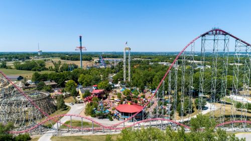 Aerial view of a vibrant amusement park featuring roller coasters, rides, and green trees under a clear blue sky.