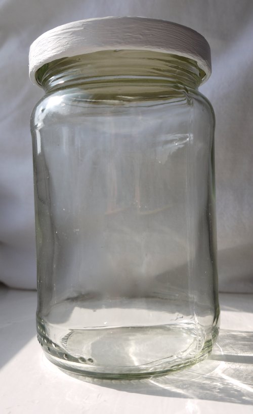 A clear glass jar with a white lid, sitting on a surface with soft lighting.