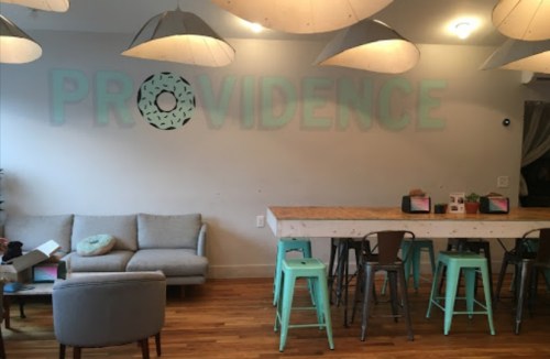 A cozy café interior featuring a "PROVIDENCE" wall sign, wooden tables, and modern seating with pendant lights.