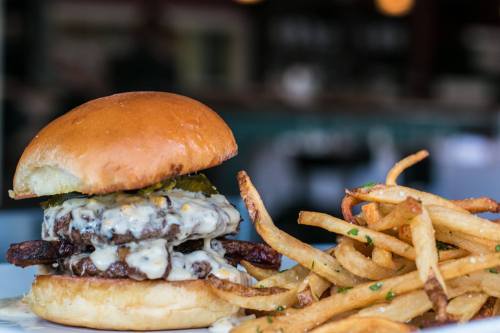 A juicy double cheeseburger with melted cheese and pickles, served with a side of crispy French fries.