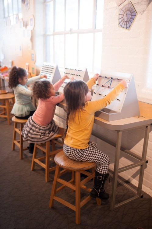 Three children engaged in a hands-on activity at a table, manipulating colorful strings on interactive boards.