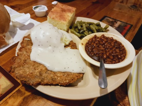 A plate of fried chicken topped with white gravy, served with green beans, baked beans, and cornbread.