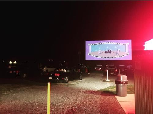 A drive-in theater at night with cars parked and a large screen displaying "Assorted Tasty Candy."