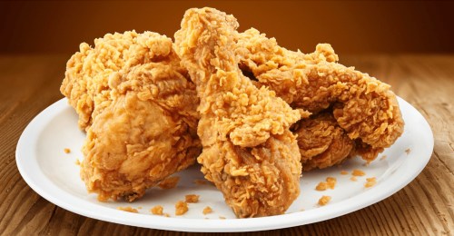 A plate of crispy, golden-brown fried chicken pieces on a wooden surface.