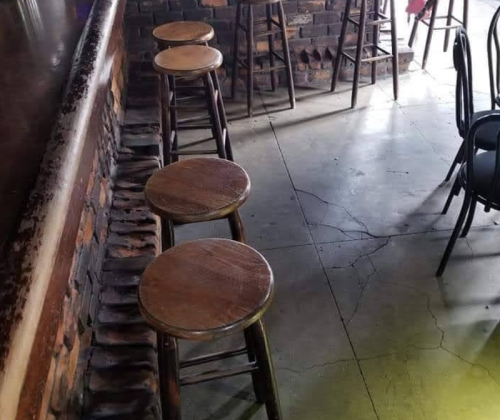 A row of wooden bar stools lined up against a brick wall in a casual setting.