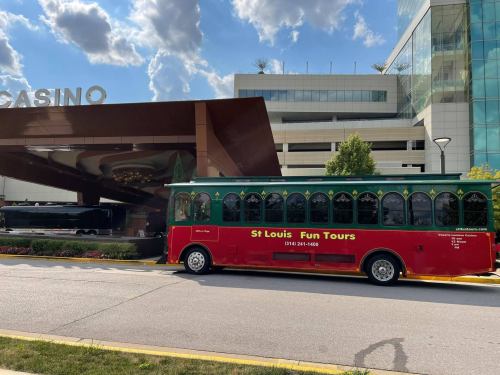 A green and red trolley bus parked outside a casino entrance on a sunny day.