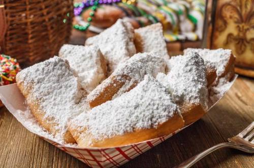A tray of freshly made beignets dusted with powdered sugar, set on a rustic wooden table.
