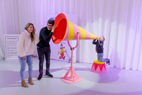 A woman and a man listen to a large colorful megaphone while a child plays with another megaphone nearby.